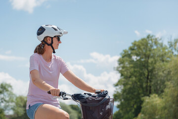 A woman enjoys a leisurely bike ride under a clear blue sky in a park, wearing sunglasses and a...