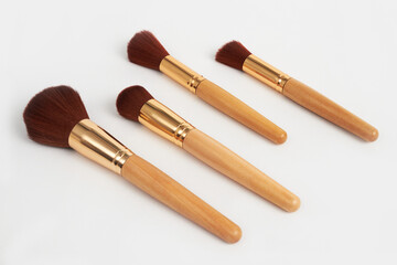 Four makeup brushes with wooden handles and golden ferrules lying on white background