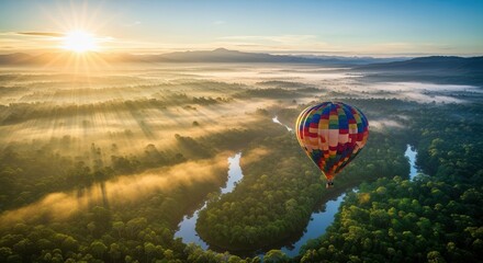 Fototapeta premium A hot air balloon floats over a river and forest at sunrise with fog and mountains in the distance