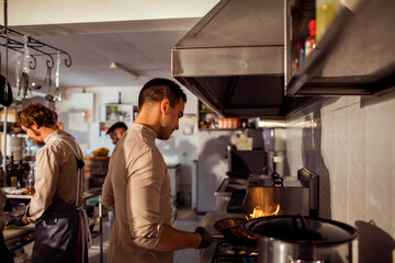 Young chef cooking food on gas stove with open flame in restaurant kitchen