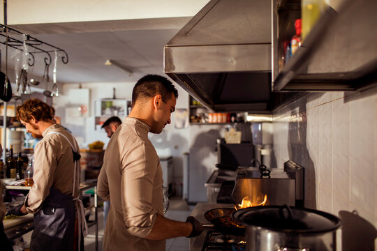 Young chef cooking food on gas stove with open flame in restaurant kitchen