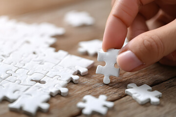 Hand of male trying to connect pieces of white jigsaw puzzle on wooden table. Healthcare for alzheimer disease, dementia, memory loss, autism awareness and mental health concept