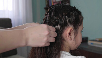 Naklejka premium Person is braiding young girl hair in cozy indoor setting, creating intricate braids that enhance her hairstyle with care and precision, evoking sense of tenderness and attention to detail