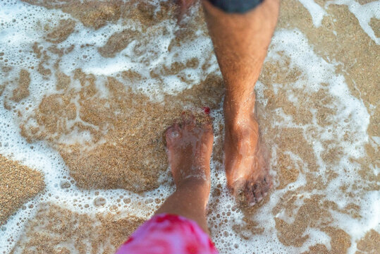 Couple standing barefoot on the beach enjoying the ocean waves