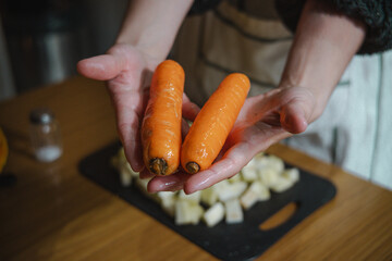 Anonymous woman holding two carrots in the foreground in her kitchen.