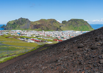 Hikers on the long climb up the lava around the crater of Eldfell, the volcano with town and harbor...
