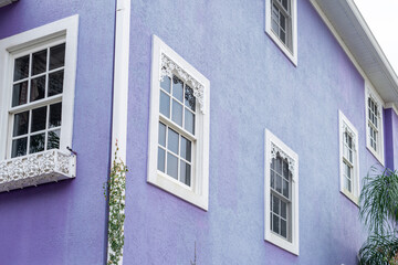 The exterior corner of a large purple building with a stucco exterior finish and multiple single-hung glass windows. The trim and crossheads above the windows are a decorative white wooden design.