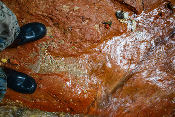 Walking in rubber boots on red clay at the bottom of a stream