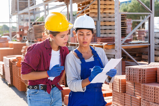 Two female storekeepers working in a building materials store are discussing important work issues in the warehouse, holding ..an estimate in their hands
