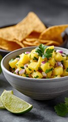 Delicious homemade tropical fruit salad with mango pine red onion cilantro and lime wedge served with crispy tortilla chips on dark surface