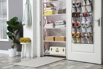 Organizer with different footwear on door, accessories and clothes indoors. Shoe storage