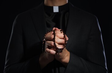 Priest with rosary praying on black background, closeup