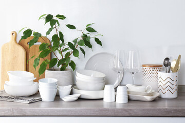 Different clean white dishware, wooden cutting boards, glasses, cutlery and houseplant on counter in kitchen