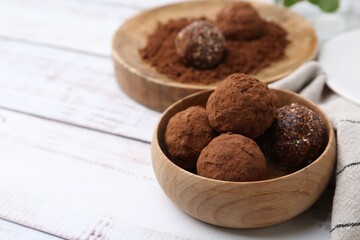 Delicious homemade candies with cocoa powder on white wooden table, closeup. Space for text