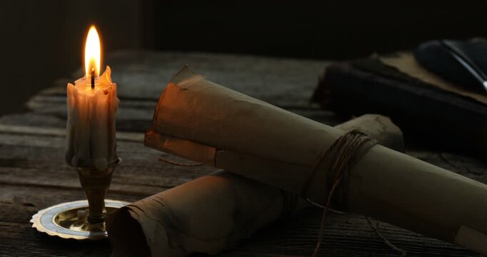Old rolled scrolls and burning candle on wooden table, closeup