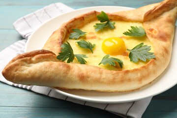 Tasty khachapuri with cheese, egg and parsley on light blue wooden table, closeup