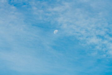 High cloud in the blue afternoon sky with a partial moon rising
