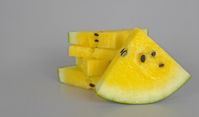 Sliced yellow watermelon.Several rectangular slices of yellow watermelon are stacked precariously. Slices of yellow watermelon on a gray background. Copy the space at the top and sides.