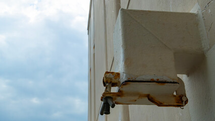 Weathered square ventilation pipe, with rusty fittings is mounted on a textured wall
