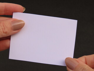 Closeup of woman hands holding white card on black background.