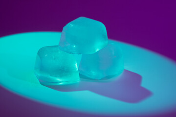 A striking photo of three ice cubes under blue spot and contour lights, surrounded by purple...