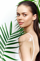 Fototapeta premium Woman applying skincare product with tropical leaves in the background, showcasing natural beauty and hydration.