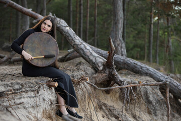 Young woman playing shaman drum in forest ritual