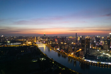 A city skyline glows with lights along a river during twilight.