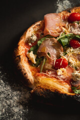 Pizza with lots of vegetables and grated cheese on a black table.