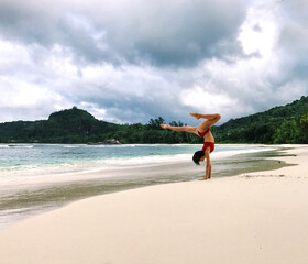 Unrecognisable young sporty woman in red swimwear doing hand stand with wide open legs and one knee...