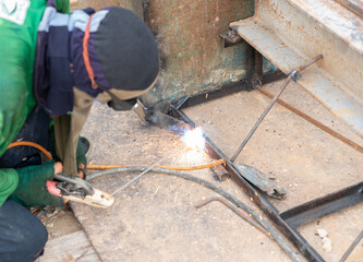 A construction worker performing manual arc welding on a metal frame structure.