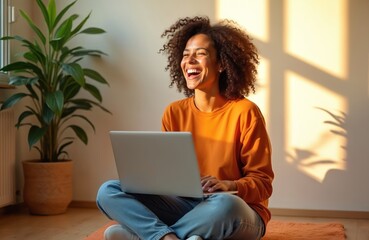 Happy woman with curly afro hair sits on floor with laptop. Wears jeans, orange shirt. Laughing talking via video call. Natural light fills room, creating warm atmosphere. Casual home office setup.