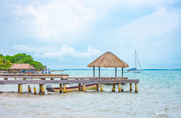 A picturesque wooden pier with thatched roofs, boats, and beautiful turquoise waters at Rosario...