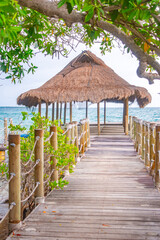 A serene wooden dock leads to a thatched roof hut, surrounded by lush greenery and beautiful ocean...