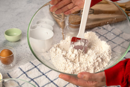 Person mixing flour in glass bowl with red spatula on kitchen counter with baking ingredients and utensils - Powered by Adobe