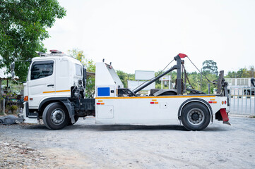 Side view of a white tow truck parked on roadside, equipped with towing gear and chains. Vehicle...