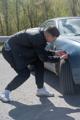 Caucasian man examines and tries to fix a deformation on the body of his car. 
