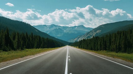Fototapeta premium Long straight open road stretching through lush green forests towards distant snow-capped mountains under a partly cloudy sky