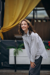 A teenage girl model is young and beautiful in a shirt and trousers on the street in a street cafe