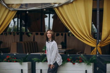 A teenage girl model is young and beautiful in a shirt and trousers on the street in a street cafe