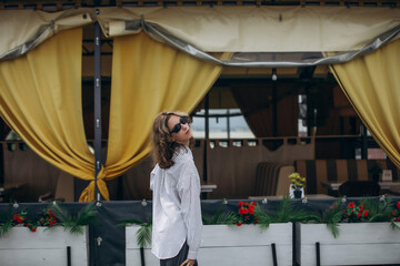 A teenage girl model is young and beautiful in a shirt and trousers on the street in a street cafe