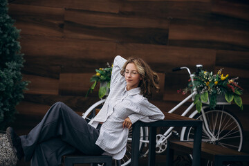 A teenage girl model is young and beautiful in a shirt and trousers on the street in a street cafe