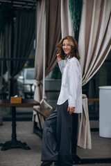 A teenage girl model is young and beautiful in a shirt and trousers on the street in a street cafe