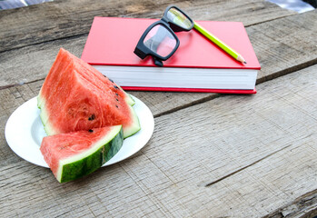 Watermelon with red book on wooden table