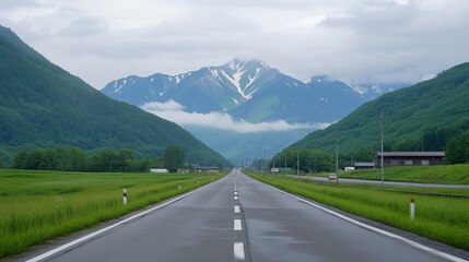 Naklejka premium Road winding through lush valley, snow-capped mountains in the distance