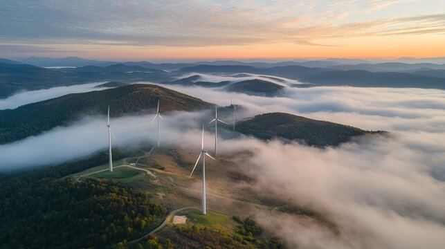 Aerial view of wind turbines atop a misty mountain range at sunrise