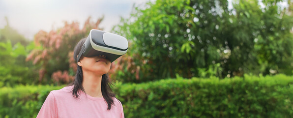 Fototapeta premium Young woman wearing virtual reality headset outdoors, female exploring VR technology in nature, person experiencing immersive digital world with modern gadget and innovation.