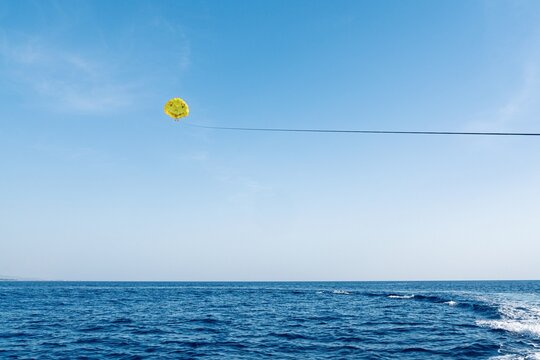 A vibrant yellow parasail glides above the clear blue sea, capturing the essence of summer fun. Ideal for travel promotions and adventure-themed projects, showcasing the thrill of parasailing.