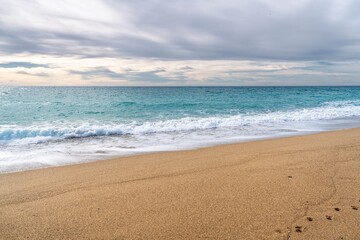 A serene beach scene with gentle waves lapping at golden sand under an overcast sky. The turquoise...
