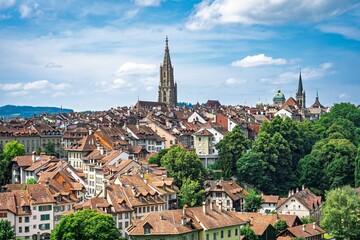 Explore the beauty of Bern, Switzerland, showcasing its charming rooftops, historical towers, and vibrant greenery under a clear blue sky. Ideal for travel and tourism promotions.